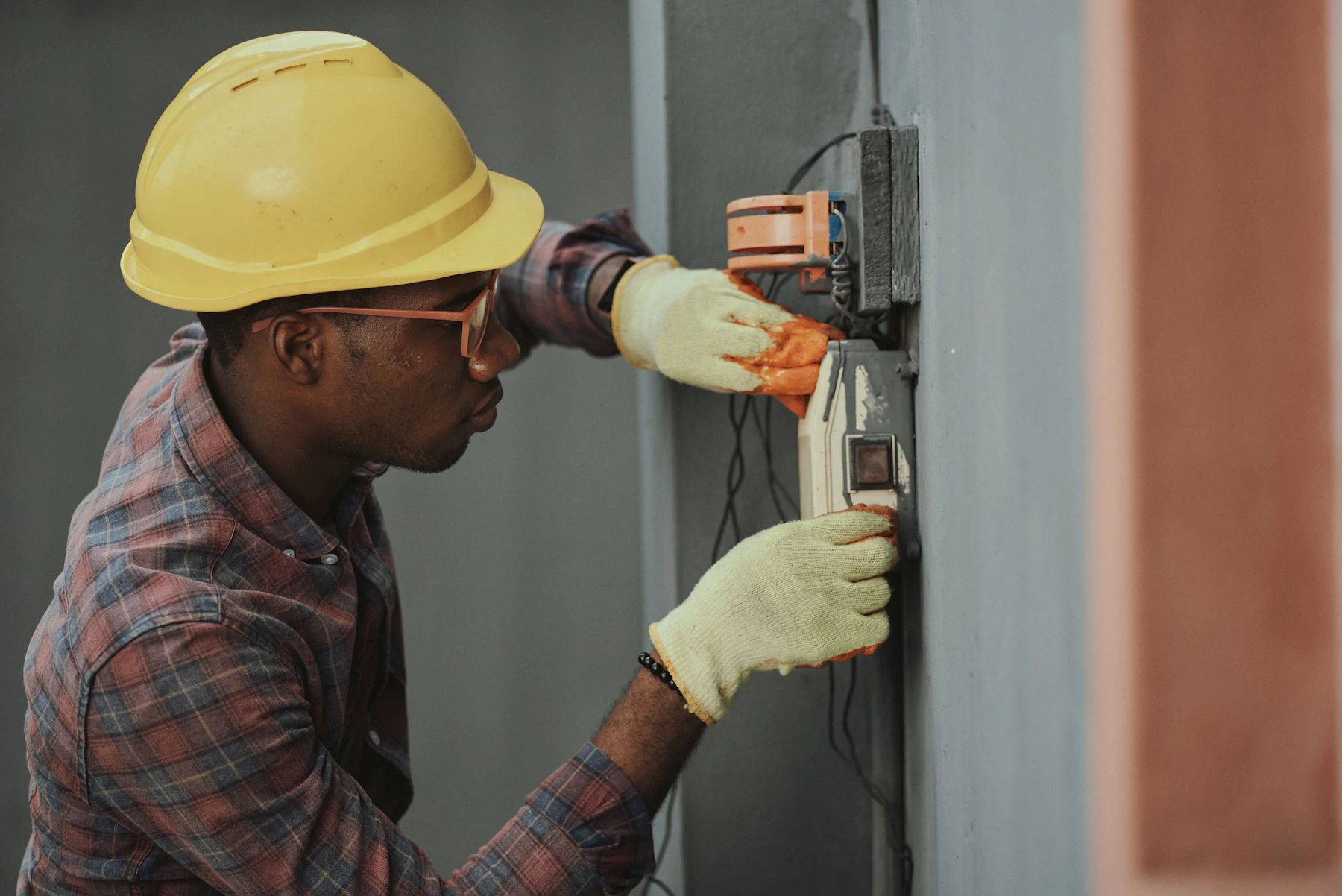 Draftline technician in a yellow hard hat testing an equipment panel with a meter